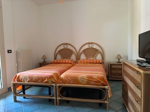 Une chambre avec deux lits, une commode, un téléviseur et un radiateur.
