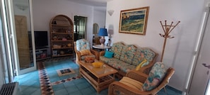 Un salon comprenant un canapé, des fauteuils, une table basse, un téléviseur, une bibliothèque et un tableau accroché au mur.