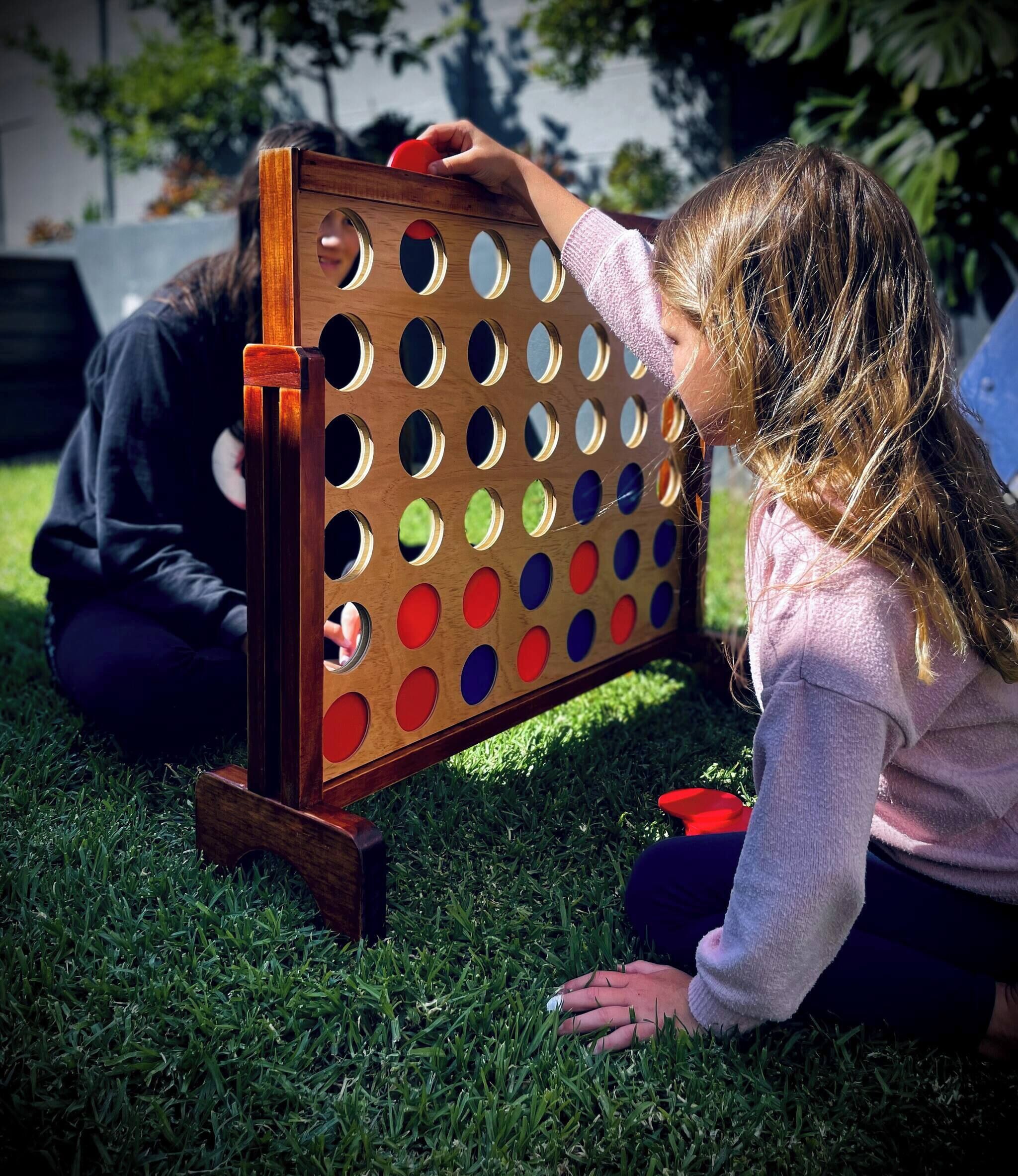 Un tablero de madera con agujeros, un objeto rojo y una persona sentada sobre césped.