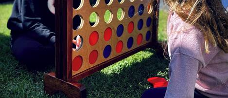Un tablero de madera con agujeros, un objeto rojo y una persona sentada sobre césped.