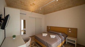Ein Schlafzimmer mit Bett, Nachttisch, Stuhl, Schreibtisch und einer kleinen Pflanze.