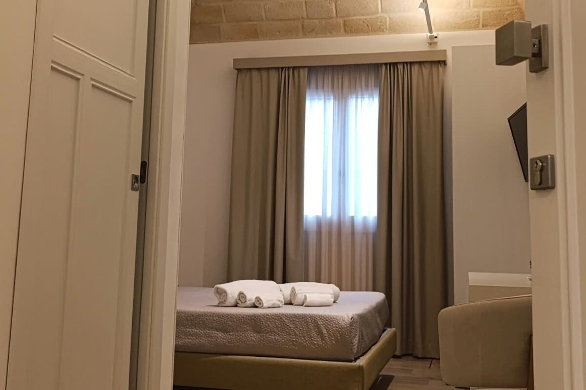 A bedroom with a bed, a chair, and a window with curtains.