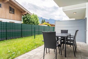 A patio with a table and chairs, a green fence, and a view of mountains. - Maiskogelblick Apartments - TOP 3, Garden & Sauna (Piesendorf)