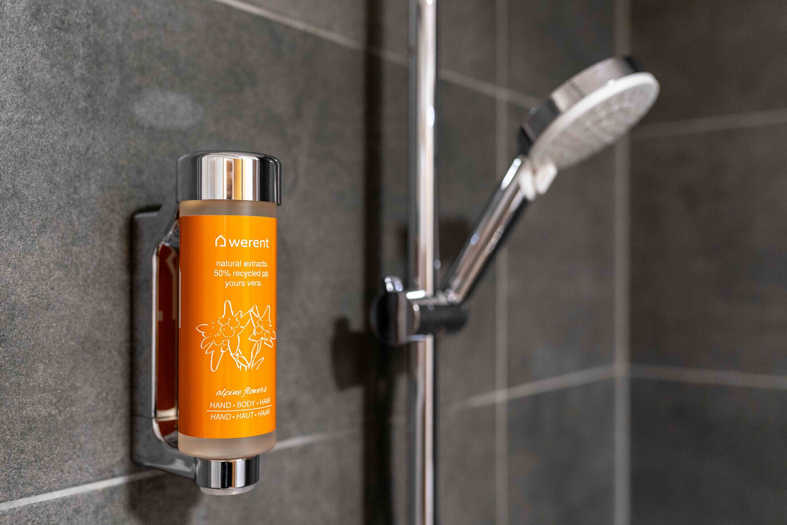A bathroom with a shower, a bottle of Alpenflora body wash, and a towel rack.
