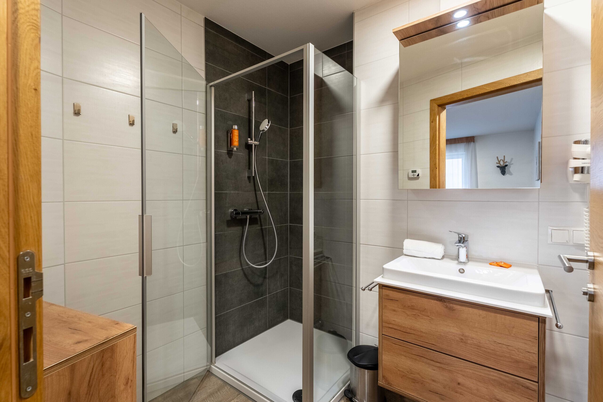 Une salle de bain avec une douche à parois de verre, un lavabo blanc et des meubles en bois.