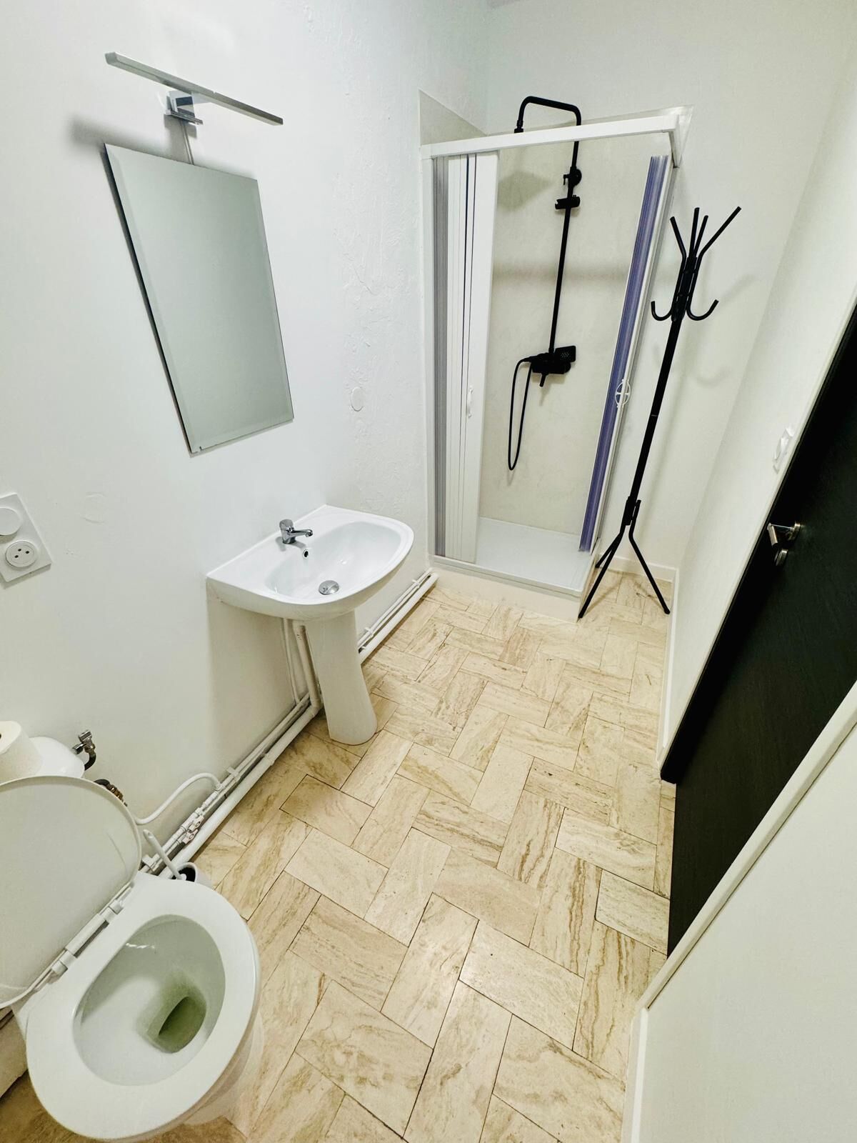 A bathroom with a toilet, sink, mirror, shower, and a herringbone-patterned floor.