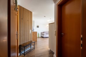 Ein Korridor mit einer Holzbank, einer Holzwand und einer Tür zu einem Wohnbereich mit Sofa und Couchtisch.