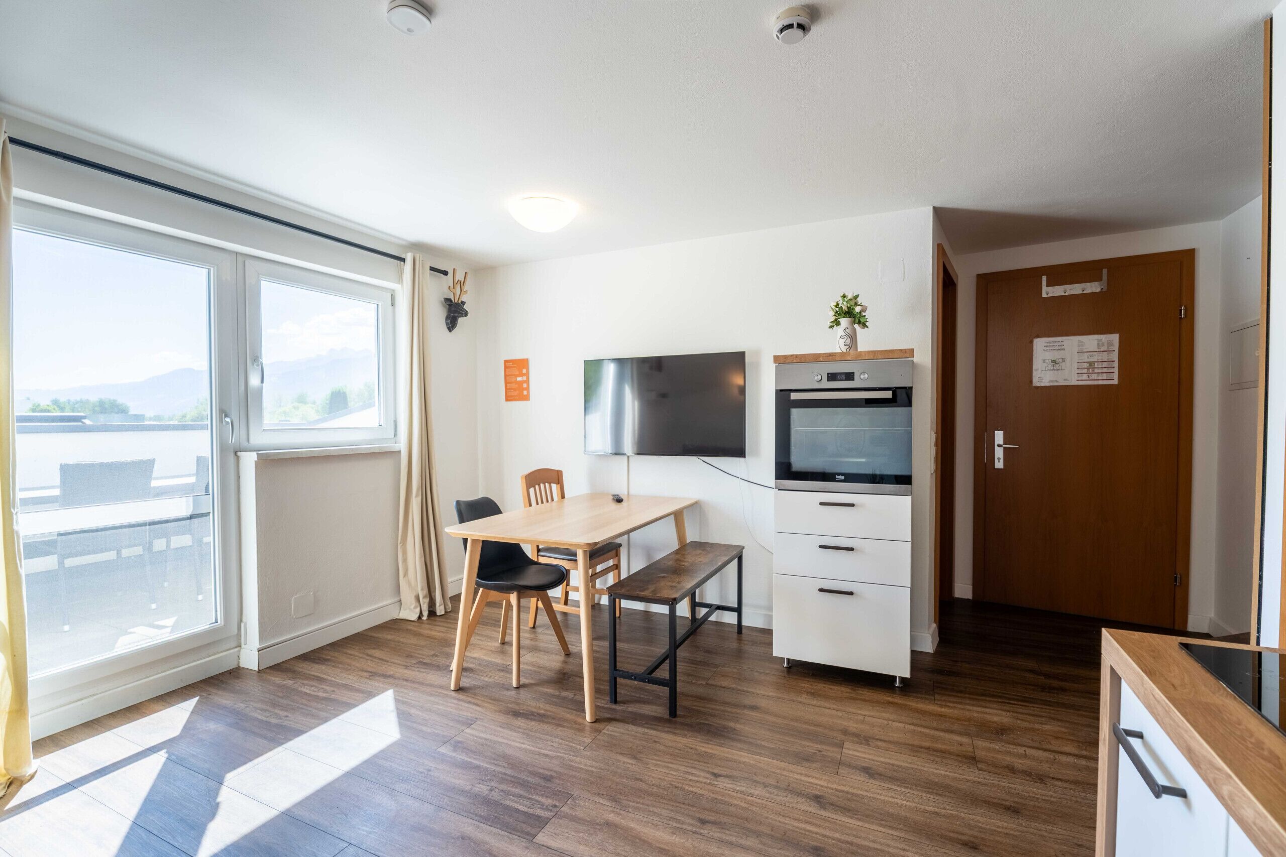 A room with a dining table, chairs, a TV, a microwave, and a wooden door.