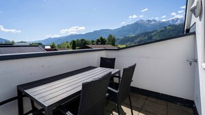 Un balcon avec une table et des chaises, une vue sur les montagnes et un mur blanc.
