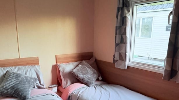 A room with two beds, a window with curtains, and a visible wall with a vent.