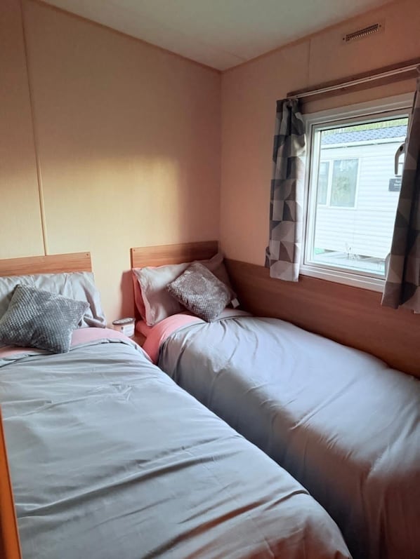 Quarto com duas camas, janela com cortinas e um painel com uma ventoinha.