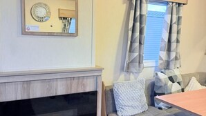 A cozy living area with a fireplace, a sofa with cushions, a wooden headboard, and a window with curtains.