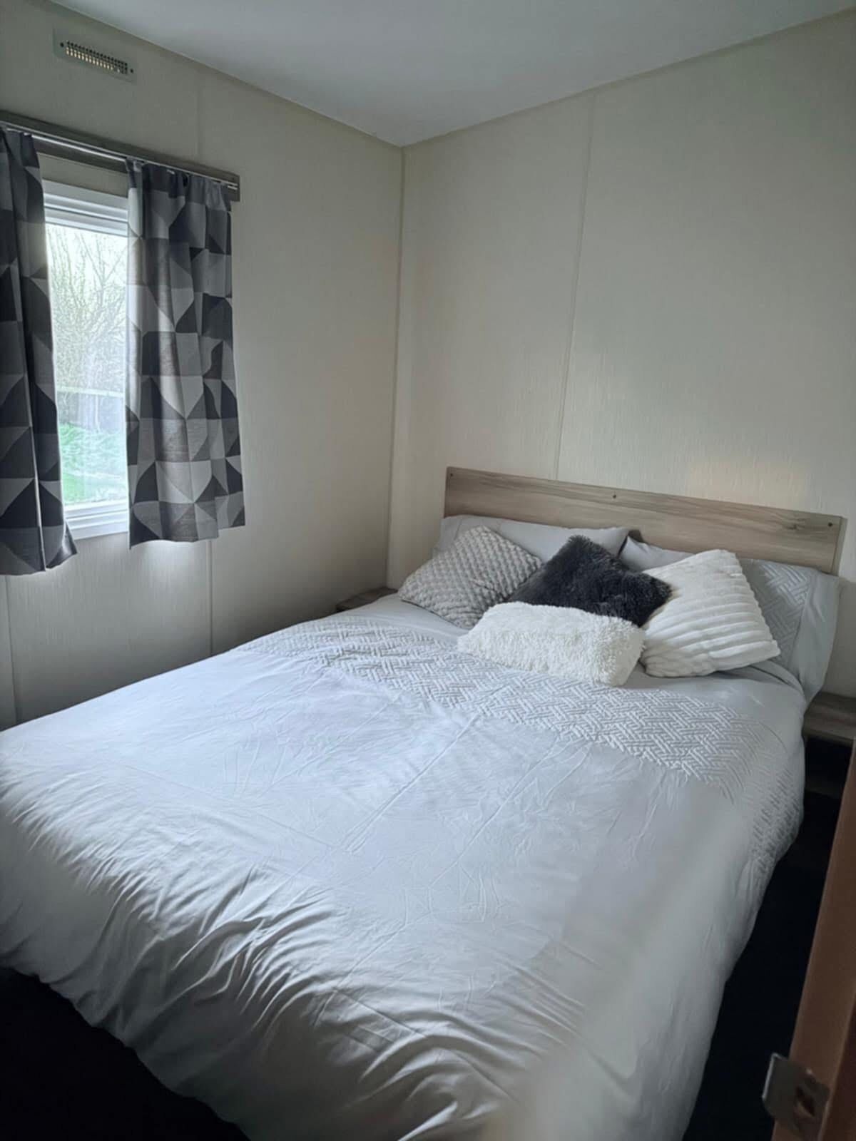 A single-bed room with a wooden headboard, a window with geometric-patterned curtains, and a plain wall.