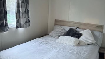 A single-bed room with a wooden headboard, a window with geometric-patterned curtains, and a plain wall.