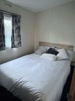 Habitación individual con una cama de madera, una ventana con cortinas de estampado geométrico y una pared lisa.