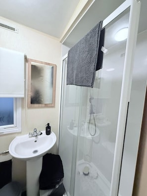 Ein Badezimmer mit einem weißen Waschbecken, einem Spiegel, einer Duschkabine aus Glas und einem Handtuch, das an der Duschtür hängt.