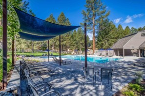 A pool area with lounge chairs, a shaded seating area, and a building in the background.