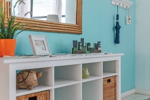 A teal wall with a 'WELCOME' sign, a mirror, and a potted plant. - Sea Breeze Sanctuary (Ormond Beach)
