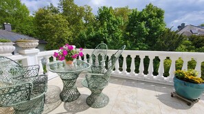 Ein Balkon mit Glastisch und Stühlen, Topfpflanzen und einem weißen Geländer.