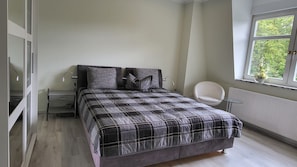 Een slaapkamer met een bed, nachtkastjes, een stoel en een raam met uitzicht.