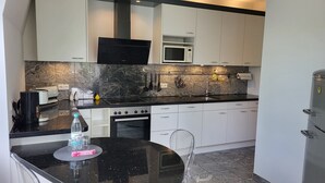 Una cocina moderna con armarios blancos, encimera negra, microondas integrado y refrigerador de acero inoxidable.