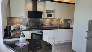 Een moderne keuken met witte kasten, een zwart aanrecht, een ingebouwde magnetron en een roestvrijstalen koelkast.