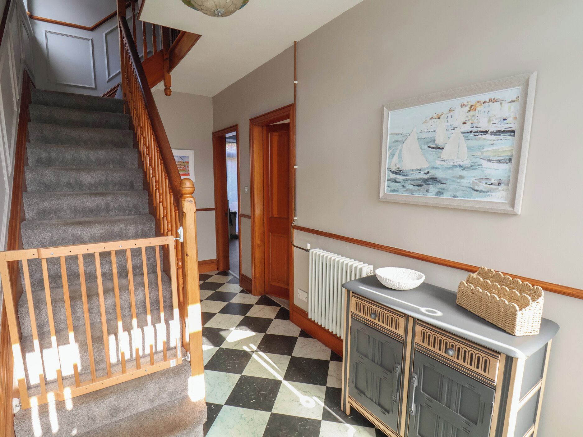 Un escalier avec une rampe en bois, un sol à carreaux, un radiateur et un tableau encadré accroché au mur.