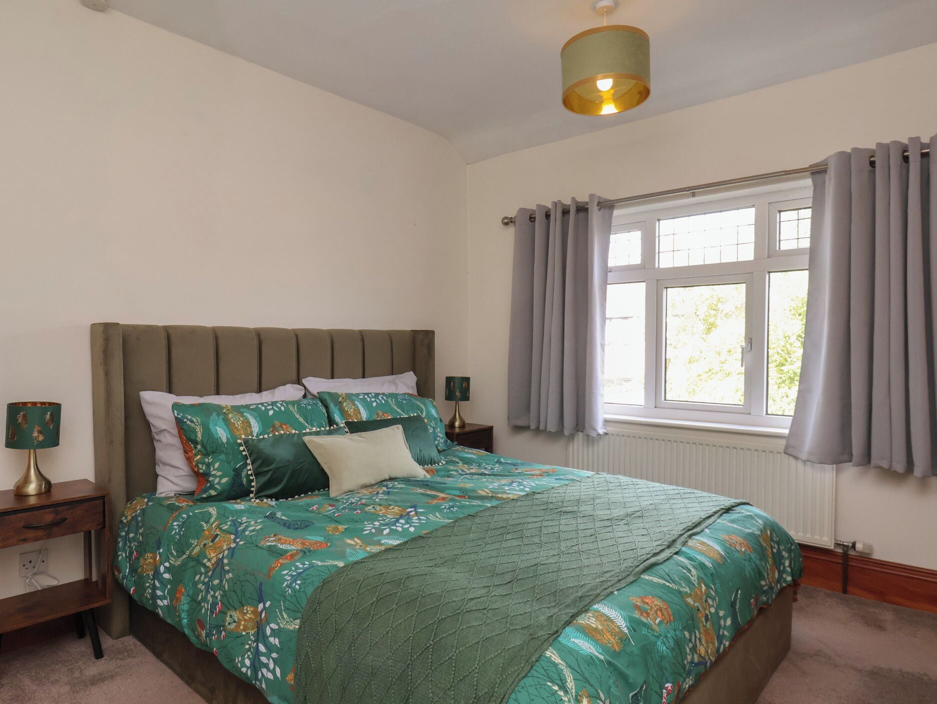 A bedroom with a bed, a nightstand, a lamp, a window with curtains, and a ceiling light fixture.