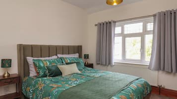 A bedroom with a bed, a nightstand, a lamp, a window with curtains, and a ceiling light fixture.