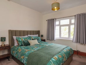 Ein Schlafzimmer mit einem Bett, einem Nachttisch, einer Lampe, einem Fenster mit Vorhängen und einer Deckenleuchte.