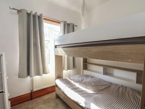 Ein Etagenbett mit Holz Kopfteil, einem fensterbepflanzten Fenster und einem Heizkörper.