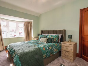 Une chambre à coucher avec un lit, des tables de chevet, une fenêtre avec des rideaux et une porte.