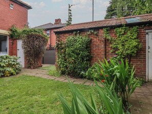 Une maison en briques avec un toit en tuiles, un jardin avec différentes plantes et une porte de garage visible.