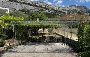 Ein gepflasterter Weg führt zu einem steinernen Torbogen, umgeben von Grünpflanzen und einer Bergkulisse.