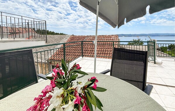 Eine Terrasse mit Tisch, Stühlen, Blumen und Blick auf das Meer und die Gebäude.