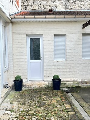 Un bâtiment avec une porte blanche, deux fenêtres et deux plantes en pot.