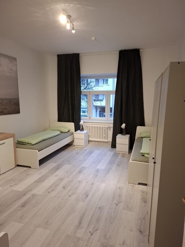 Un dormitorio moderno con cama, mesitas de noche, un radiador y una ventana con cortinas.