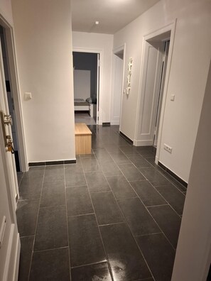 A hallway with dark tiled flooring, white walls, and a wooden bench. - Steglitz VI—Large apartment with a balcony for groups, coworkers, or families (Berlin)