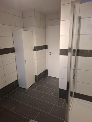 Un baño con paredes de azulejos, una zona de ducha y una puerta.