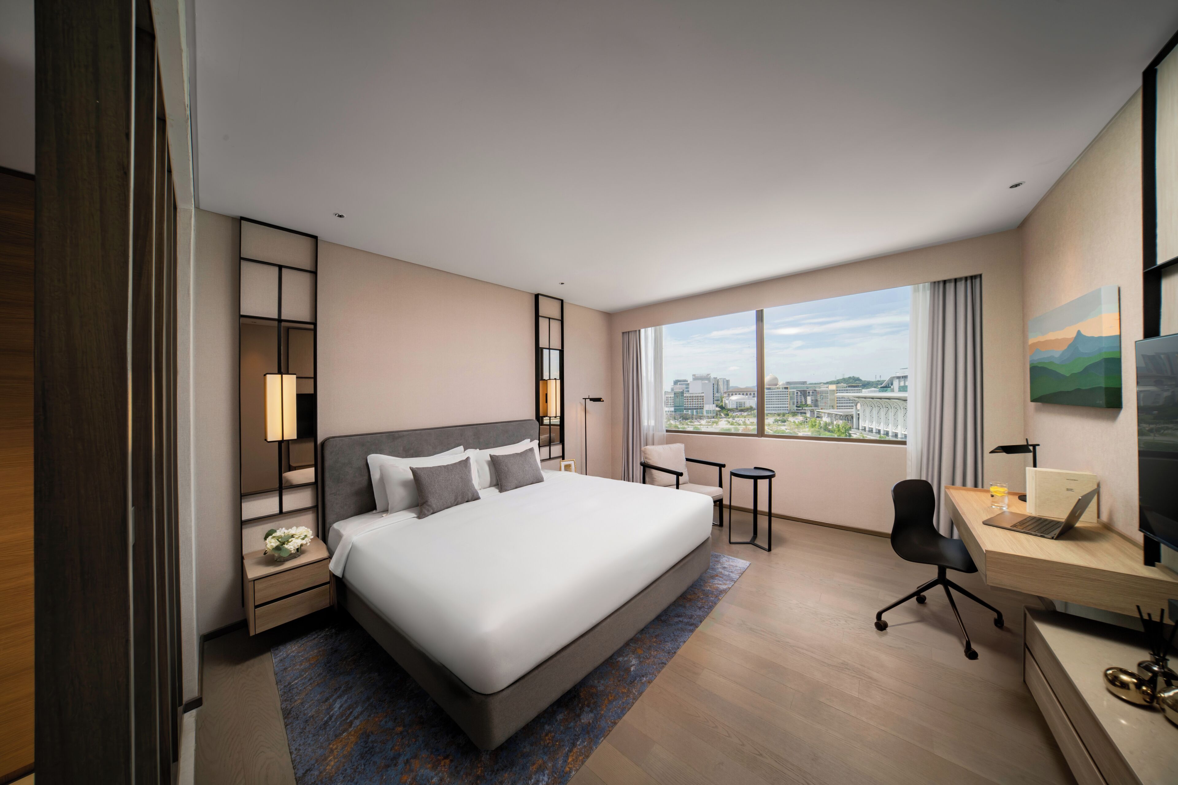 Una habitación de hotel moderna con una cama grande, un escritorio con una computadora portátil, una silla, una mesita y un televisor.