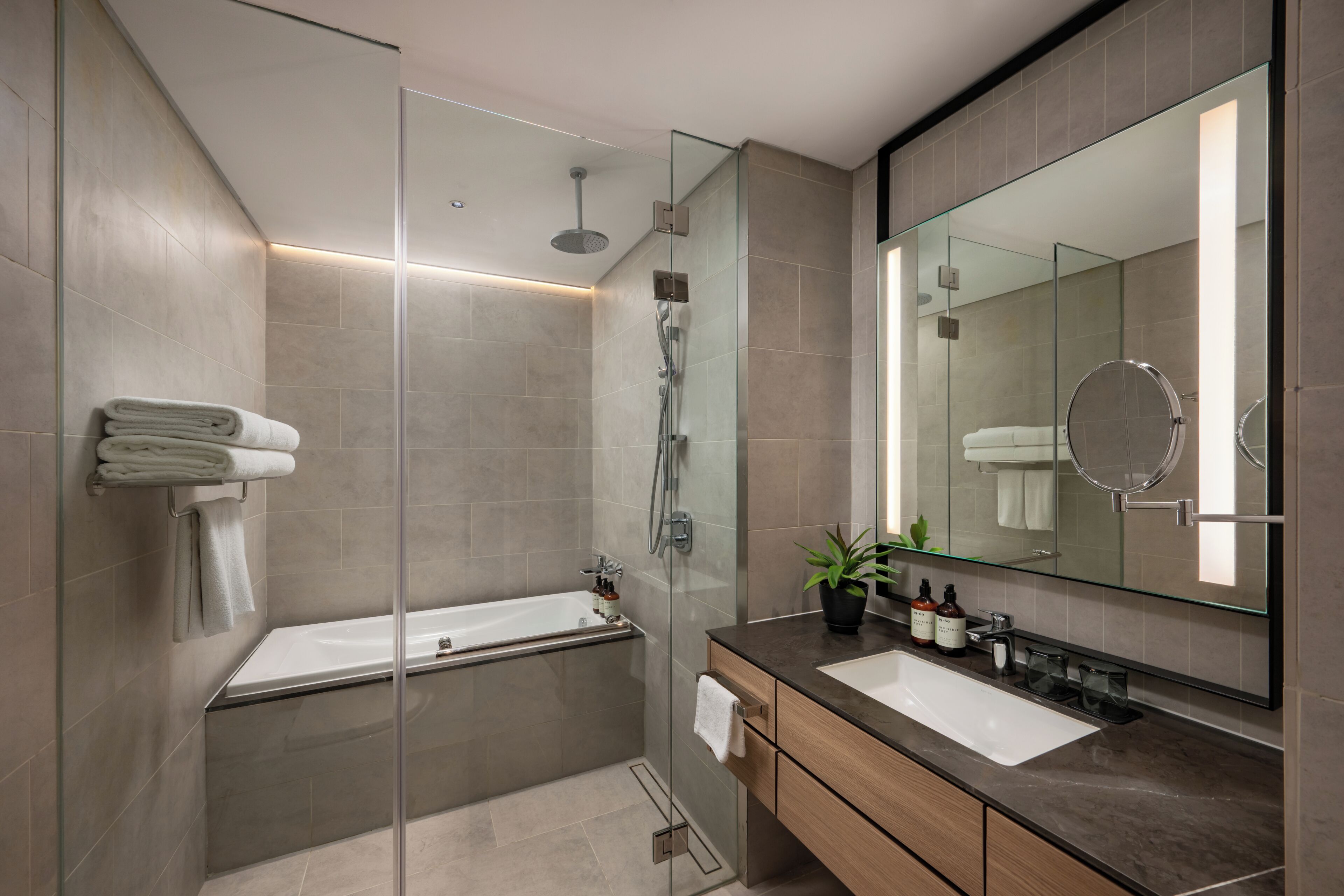 A modern bathroom with a glass shower enclosure, a bathtub, a vanity with a mirror, and a towel rack.