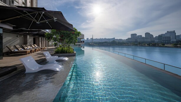 An infinity pool with lounge chairs, a city skyline view, and a river.