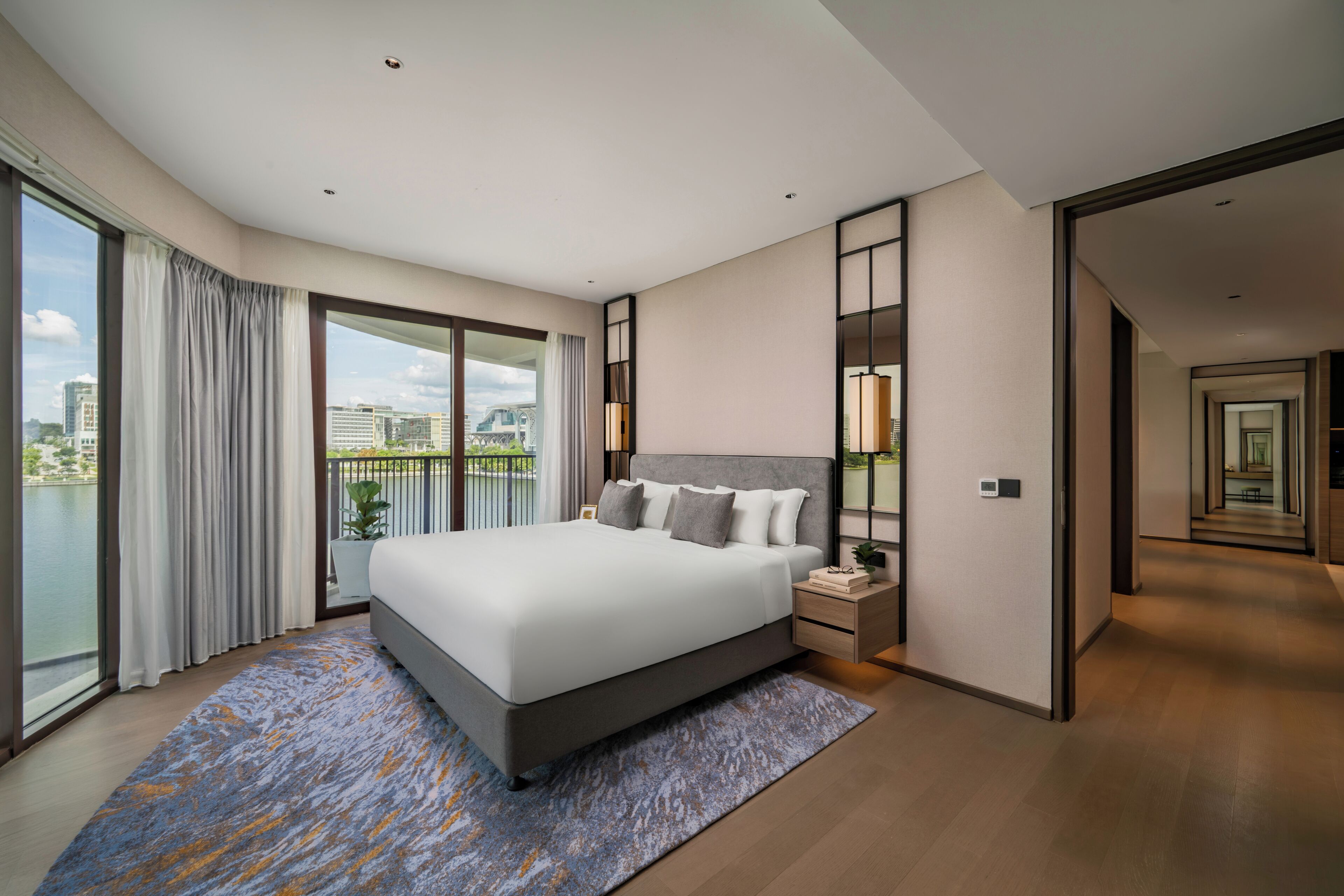 Quarto de hotel moderno com cama grande, mesa de cabeceira, vista da cidade e varanda.