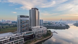 A high-rise building with a modern architectural design, a river in the foreground, and a bridge in the background.