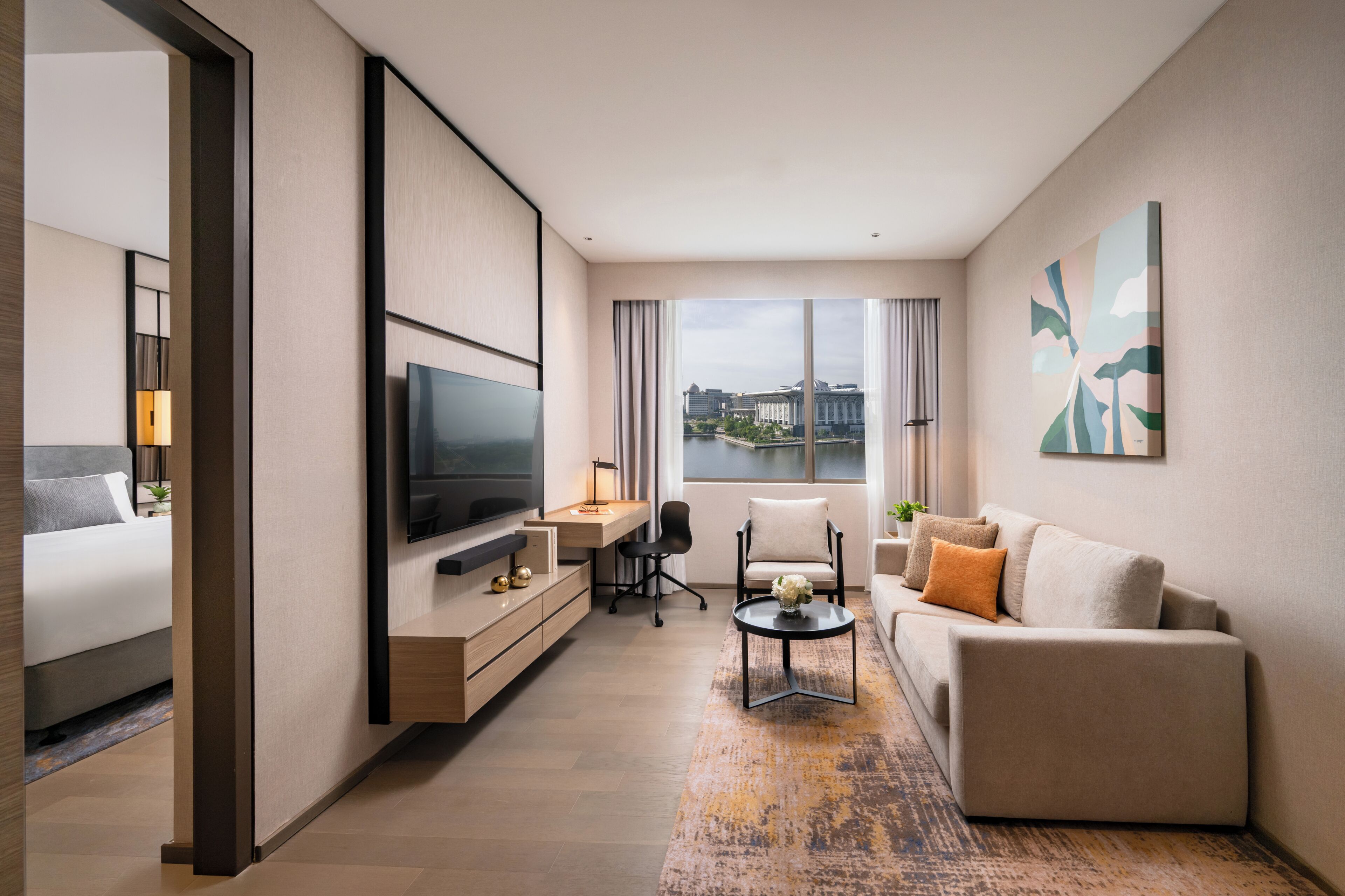 Habitación de hotel moderna con cama, televisor, escritorio, sofá y un amplio ventanal con vistas.