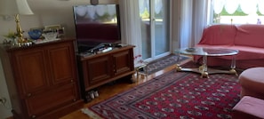 A living room with a television, wooden cabinet, glass coffee table, and a red sofa.