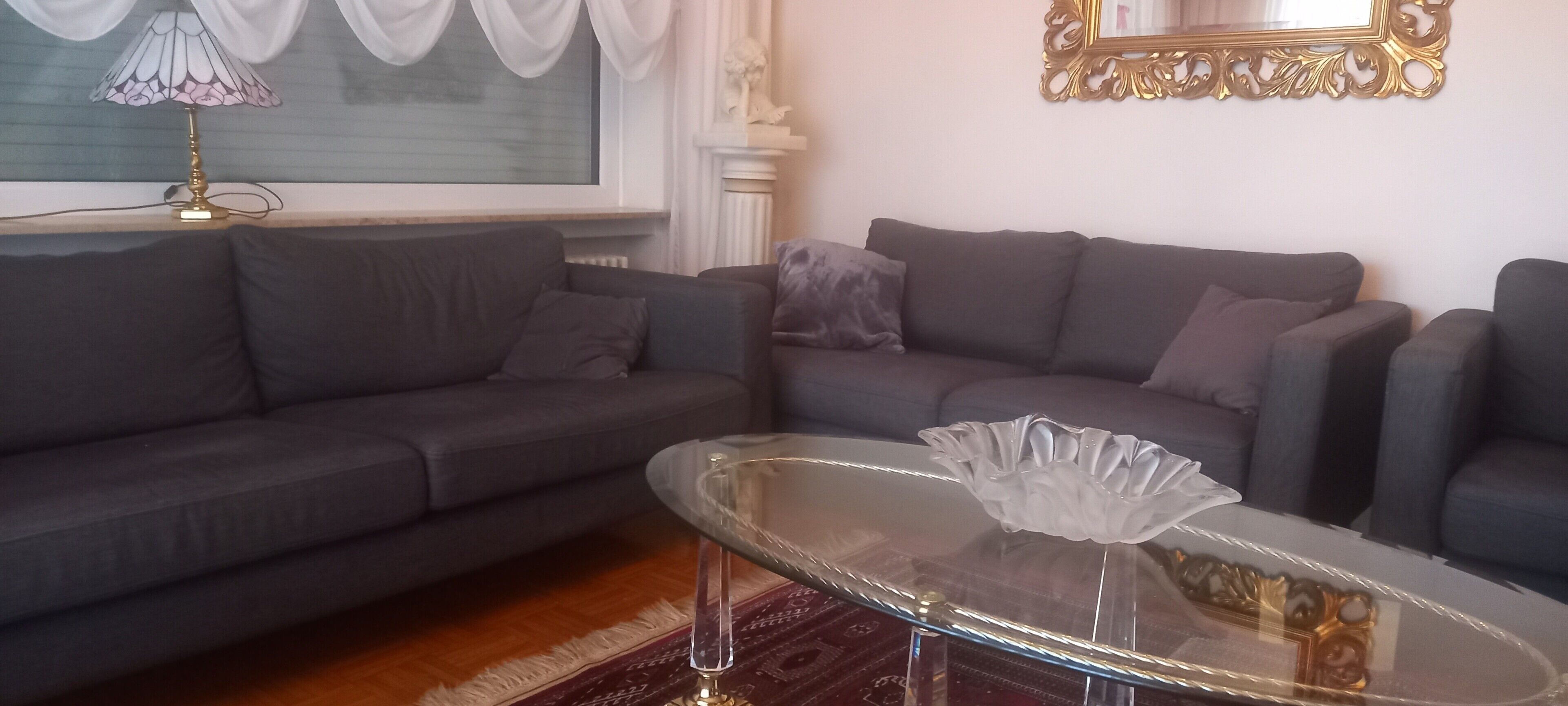 Sala de estar con dos sofás grises, una mesa de centro de vidrio y una lámpara sobre piso de madera.