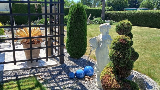 Ein Garten mit einem Metallzaun, Kübelpflanzen, einer Statue und einem gepflegten Rasen.