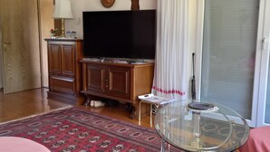 Ein Wohnzimmer mit Flachbildfernseher, Holzsäcken, einem Glastisch und einem gemusterten Teppich.