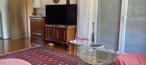 A living room with a flat-screen TV, wooden cabinets, a glass coffee table, and a patterned rug.